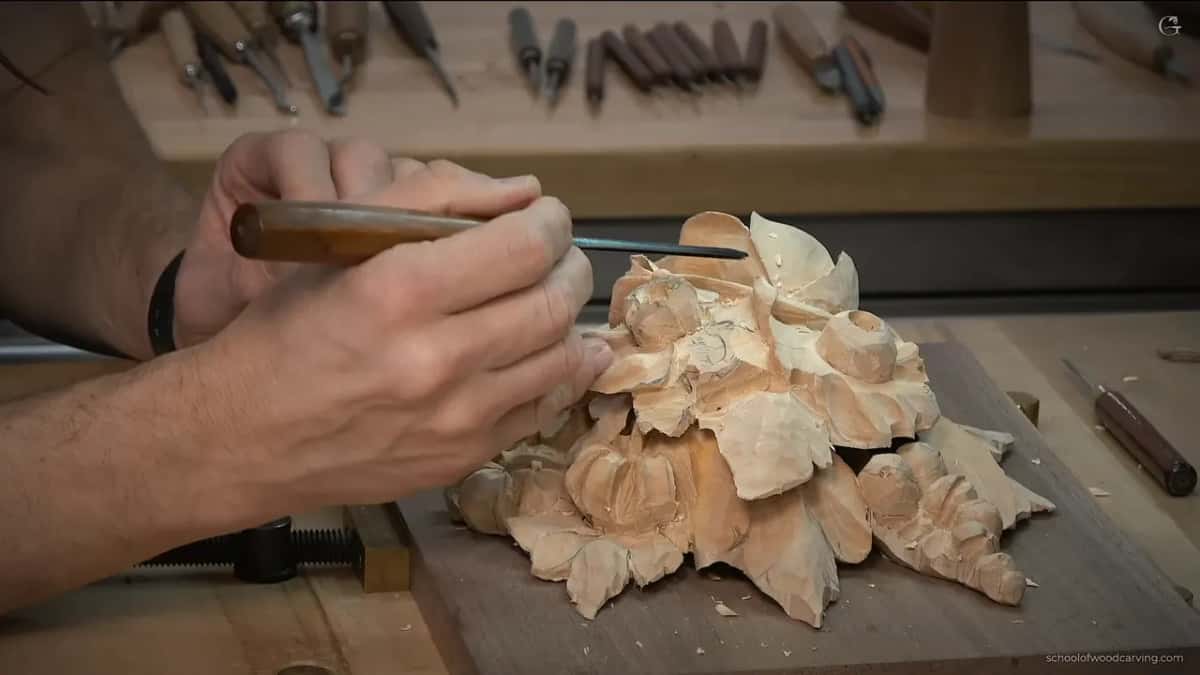 Both hands on a small detailing gouge while a rack of tools waits on the bench behind him