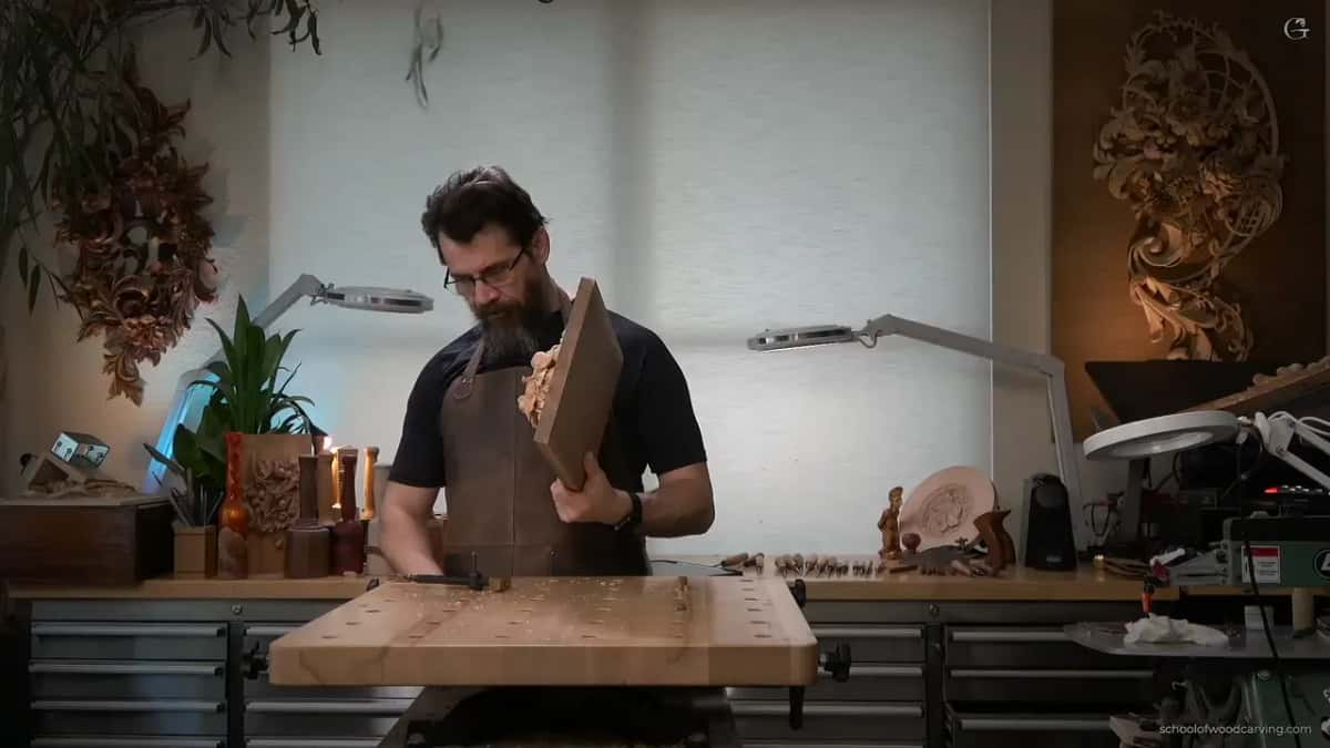 Carver holding the finished panel up on edge, other carved pieces hanging on the walls behind