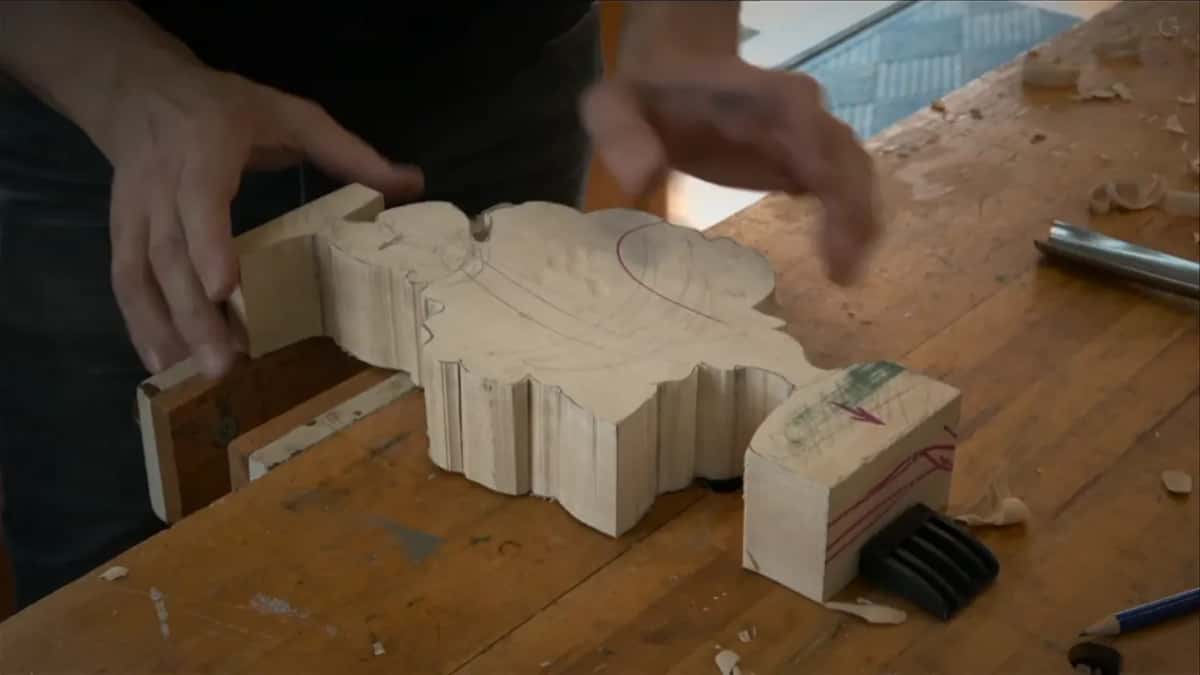 Hands turning the sawn blank over on the bench, leg tabs and red markings showing