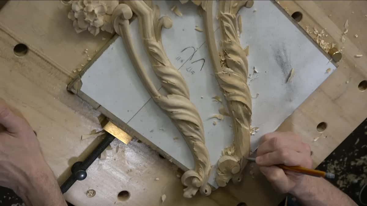 The full panel from above, with a pencil coming in at the right to redraw a movement onto carved wood.