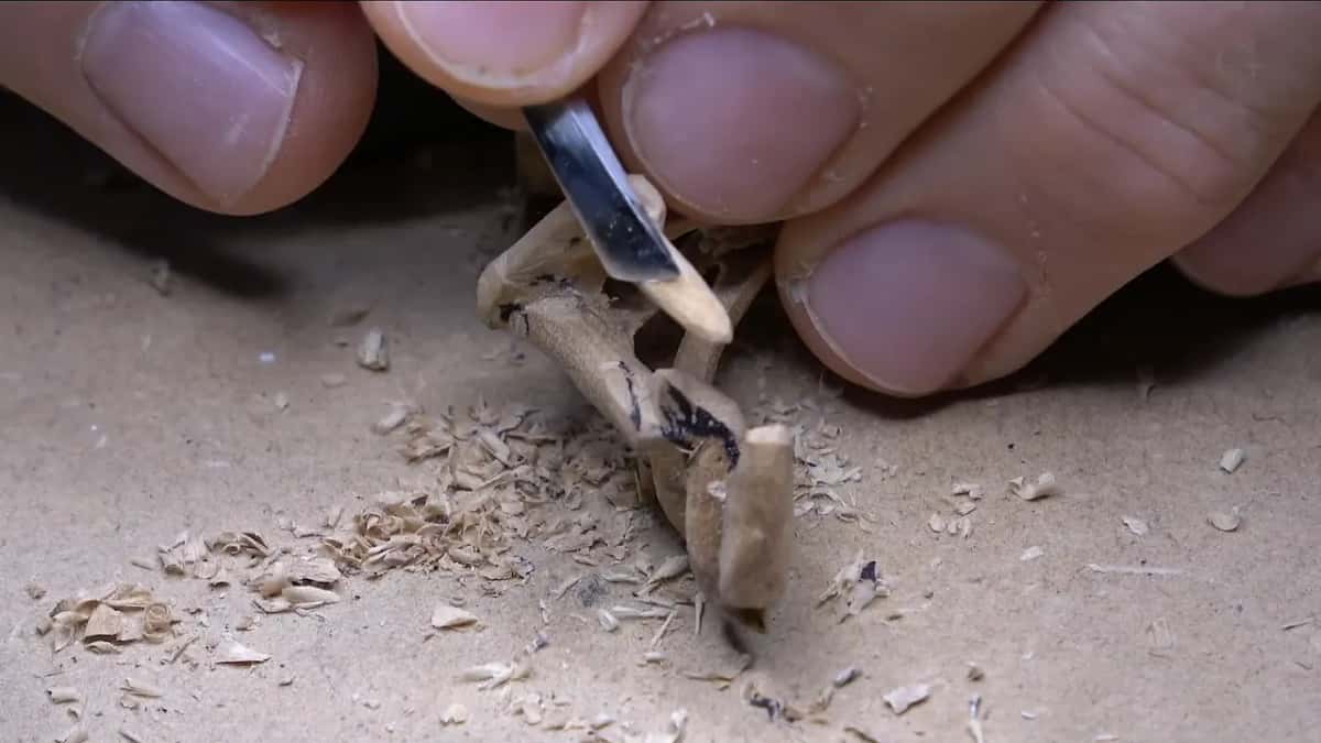 Blade tip between the thin legs, shavings piled below.
