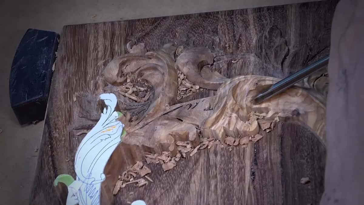 Dark box lid carved in leaves, with a white paper cutout on it and a gouge in the wood