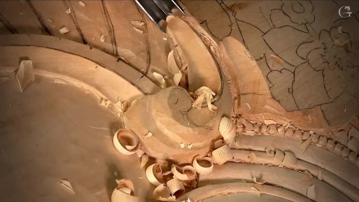 Gouge lifting one curl of wood, carved beads running down the right side