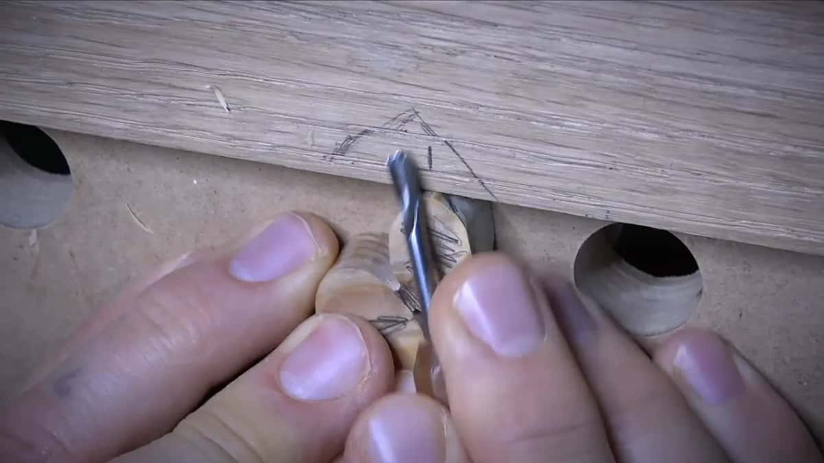 Narrow gouge easing down an olive marked in pencil, with fingers pressing it against the oak