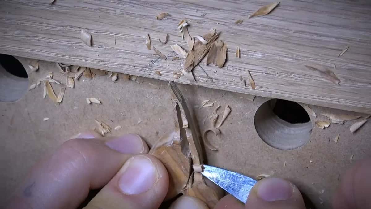 Short blade with a clear bevel shaves an olive while two fingers pin it and chips pile up behind