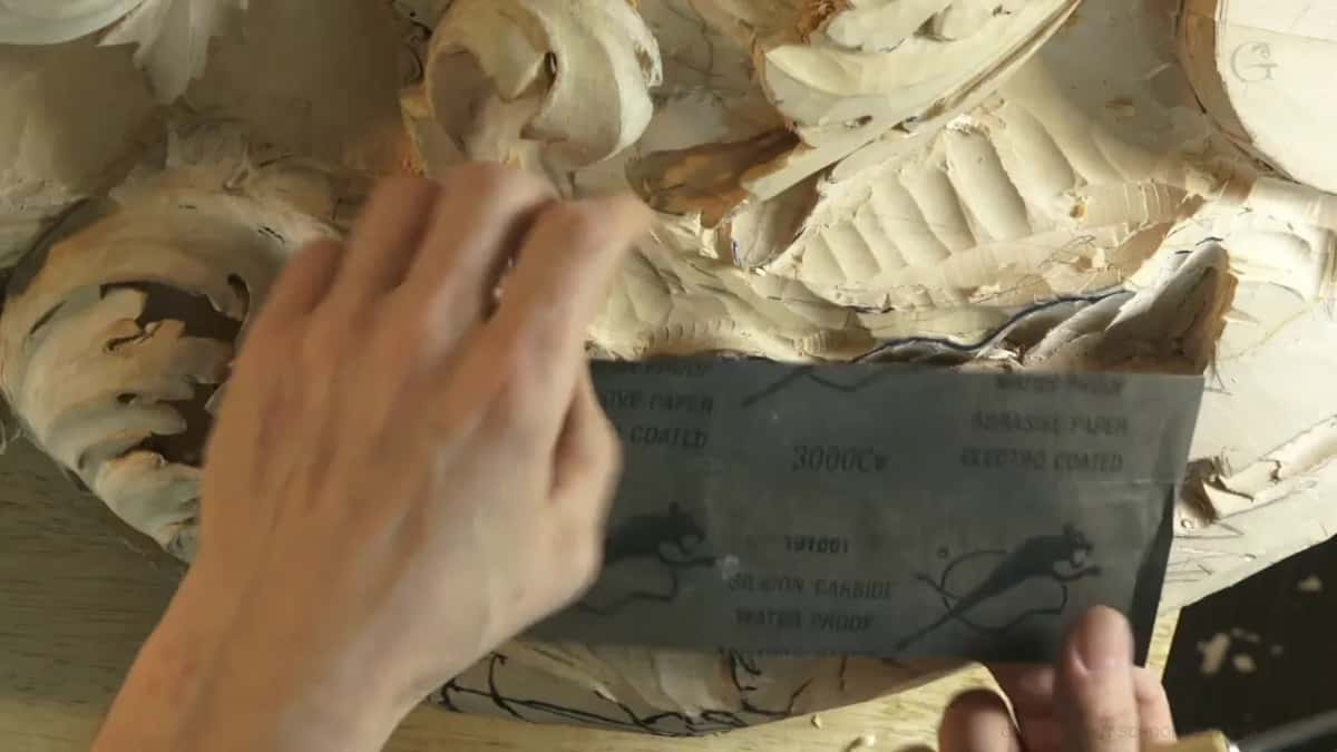 Waterproof silicon carbide paper marked 3000 held over an acanthus carving