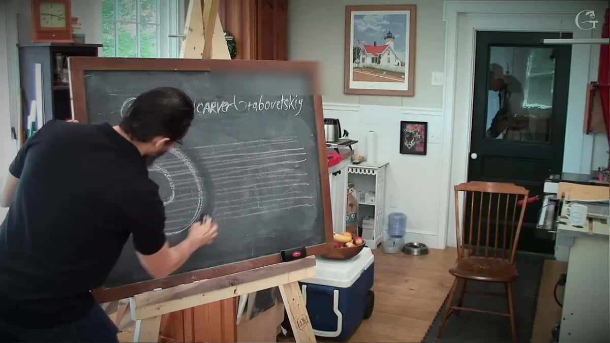 Bending to the chalkboard, he sketches the ring on top of those strokes