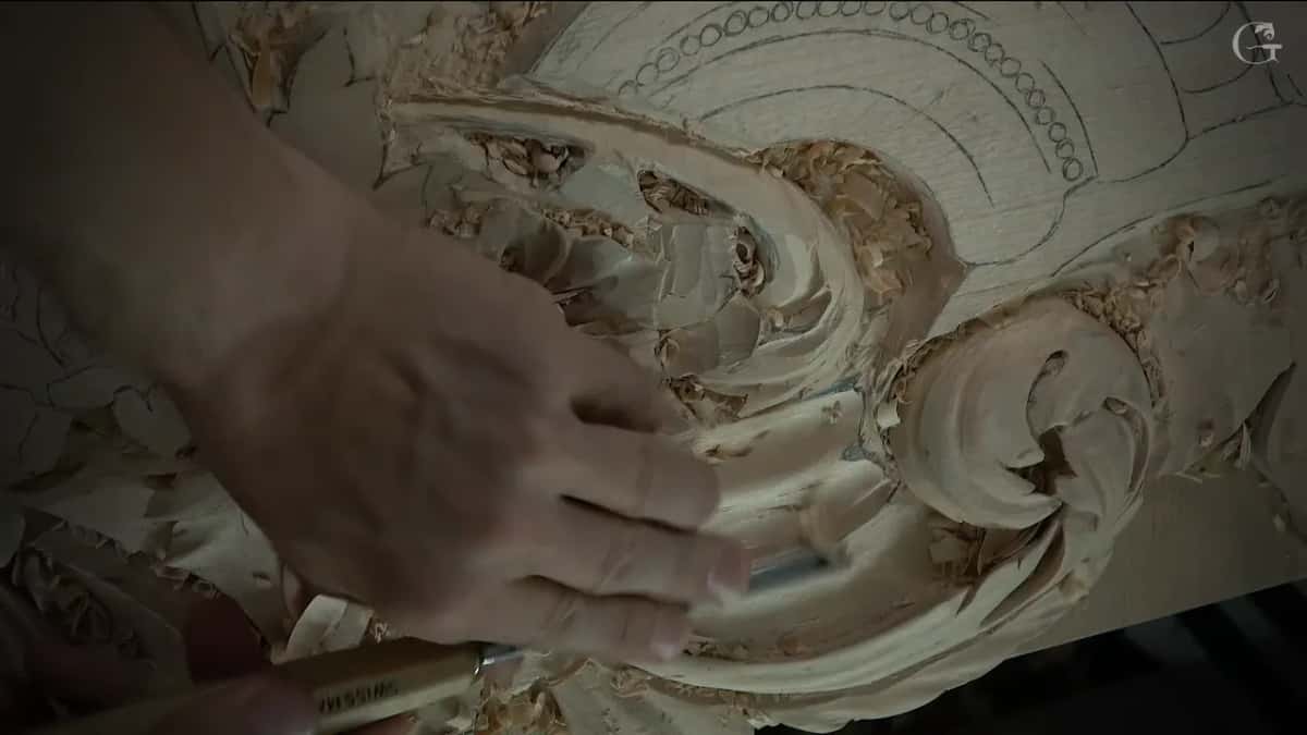 Hand spread across the carved scroll with a tool below the fingers