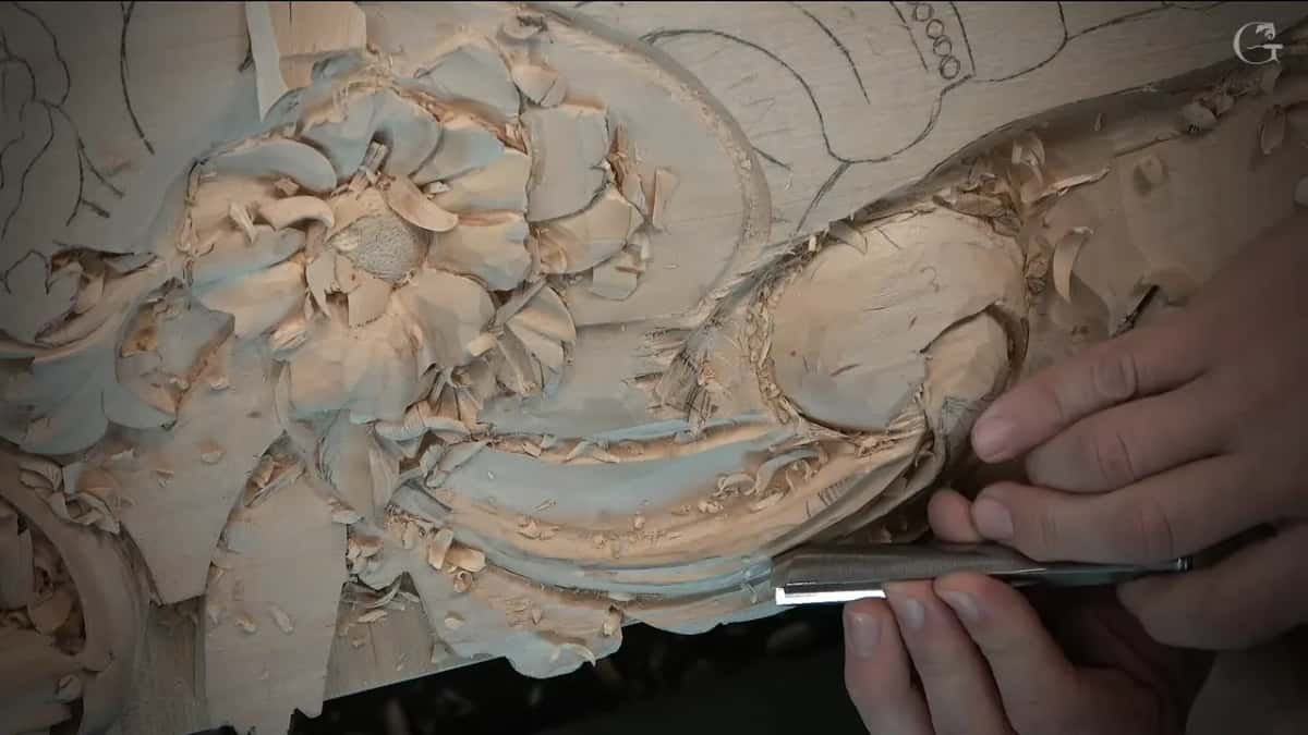 Fingers push a long gouge along the section while the flower sits just above it
