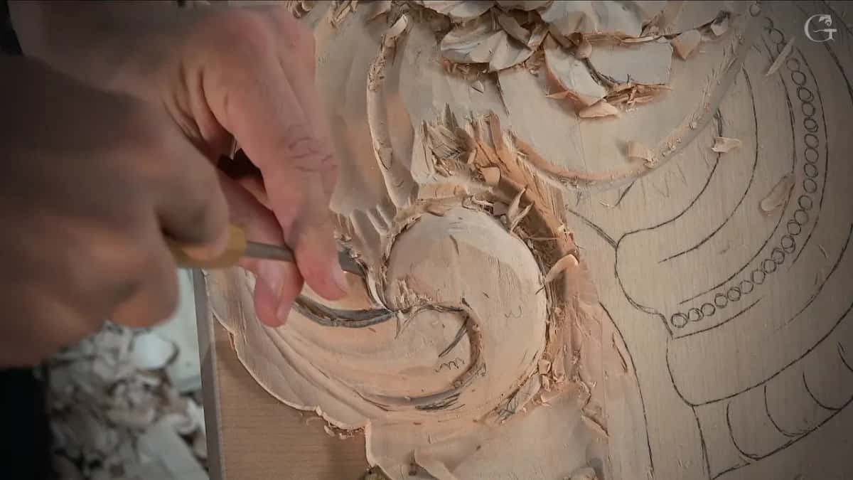 Shaping one division of the curl with a gouge, pencil circles drawn on the flat board beside it