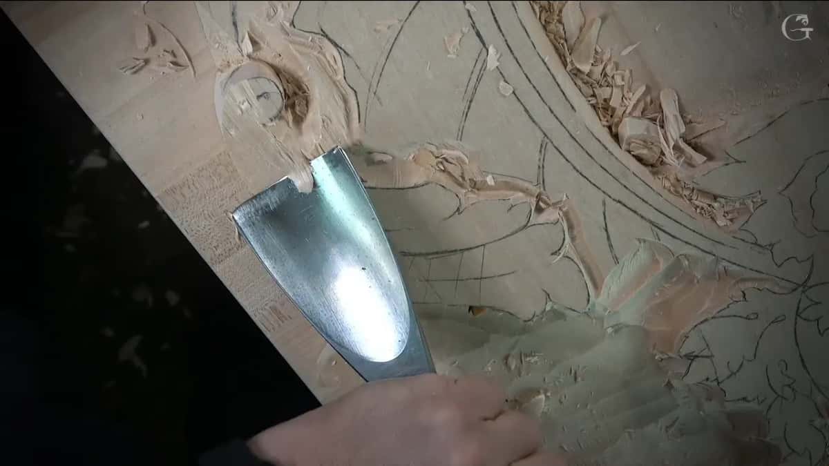 Very wide gouge set against the leaf next to the volute, its steel catching the lamp