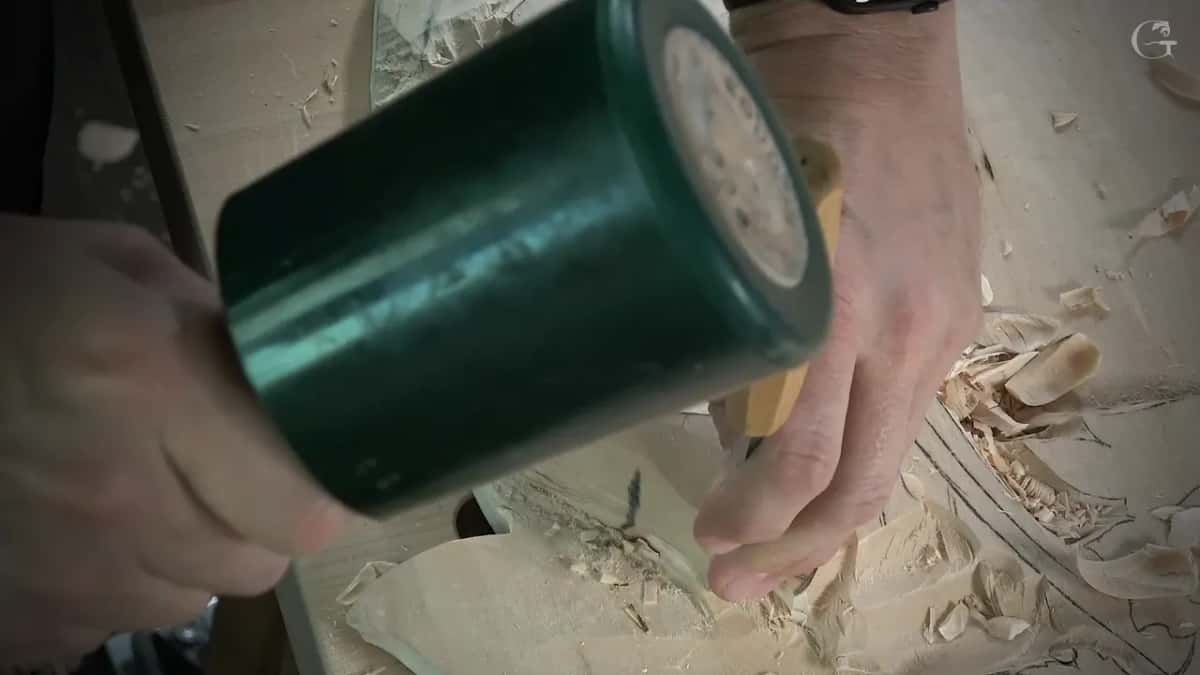 Green mallet over a gouge handle, seen close, with shavings below on the carving