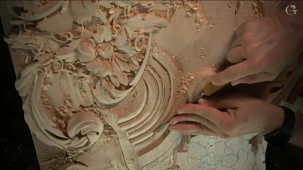 A wider view from another side, flower on the left, both hands steering a gouge at the right edge