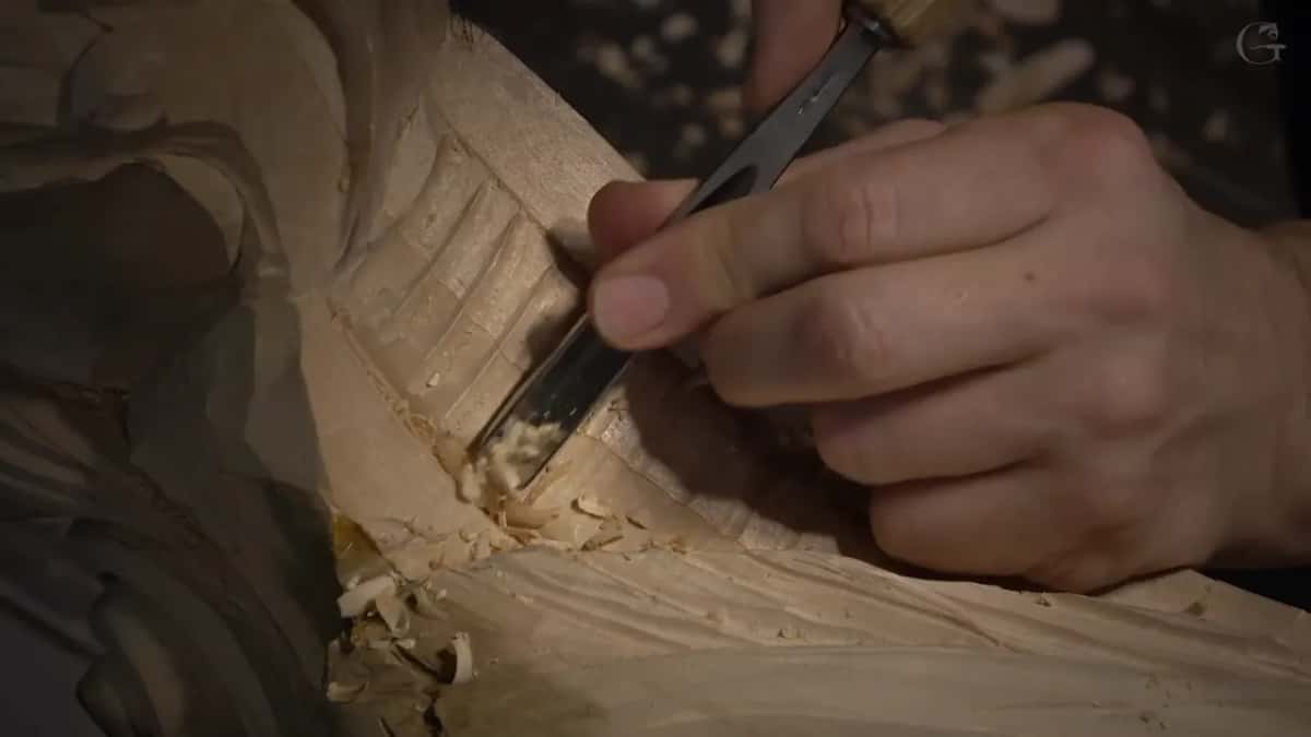 A narrow gouge cleans out the space between two shallow ribs, with fresh chips below.