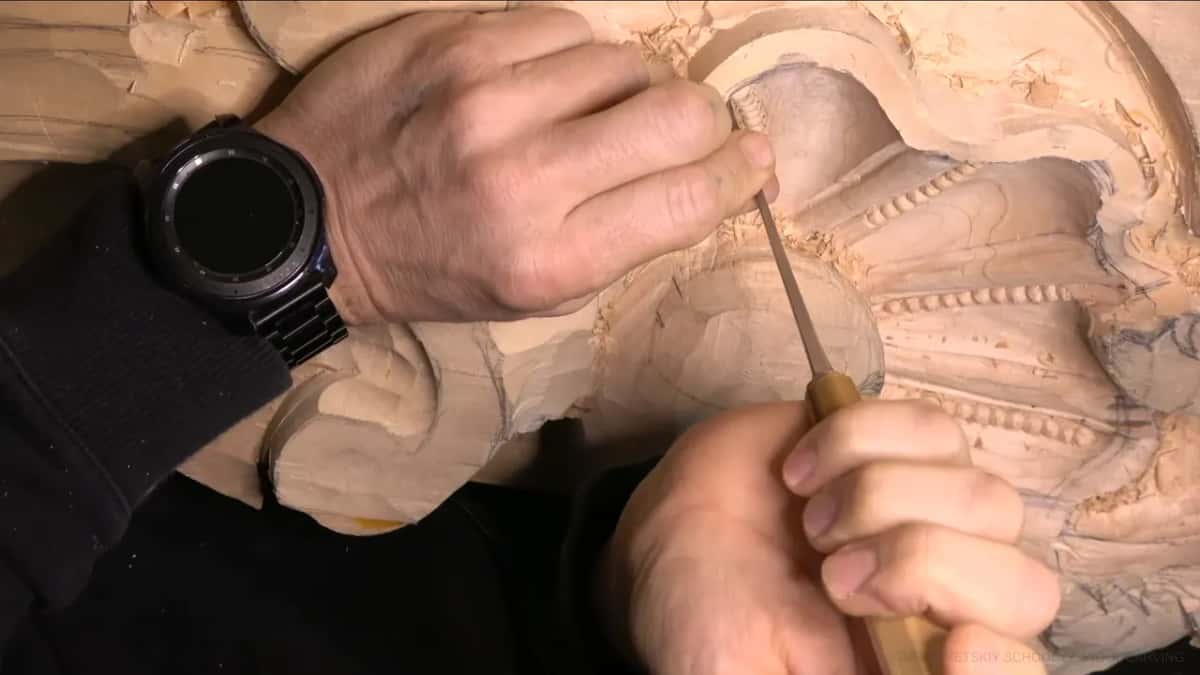 Left hand pressing down, right hand driving a gouge toward the bead border.