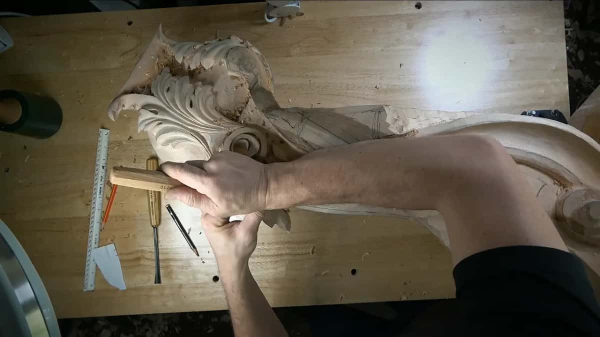 Near the scroll both hands press a gouge along the band, a ruler lying beside two tools
