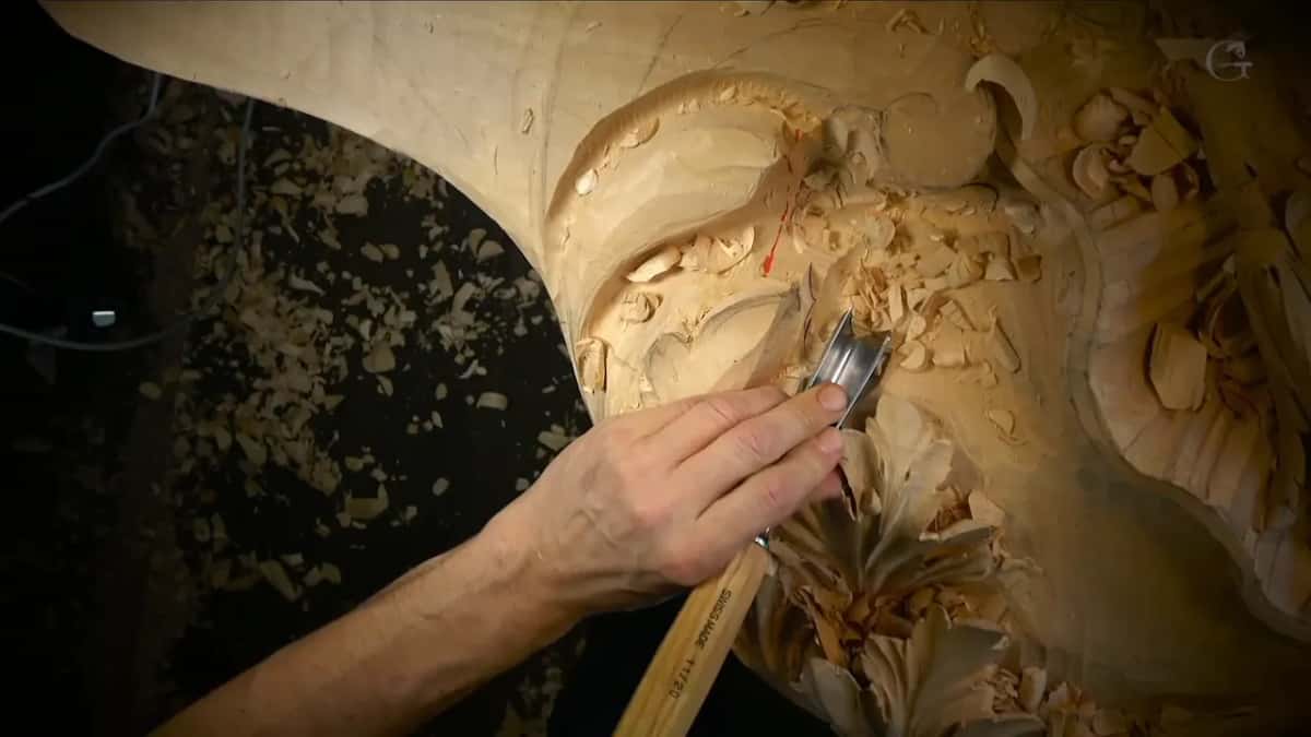 A gouge pushed into the hollow just below a round scroll, a red arrow above it.