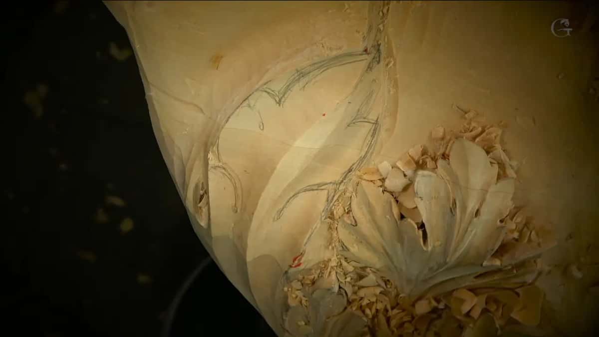 Gray pencil lines sweep over smooth wood above a carved leaf in a bed of shavings.