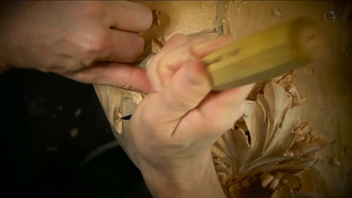 Two hands close over a yellow handle, the carved leaf just to the right.