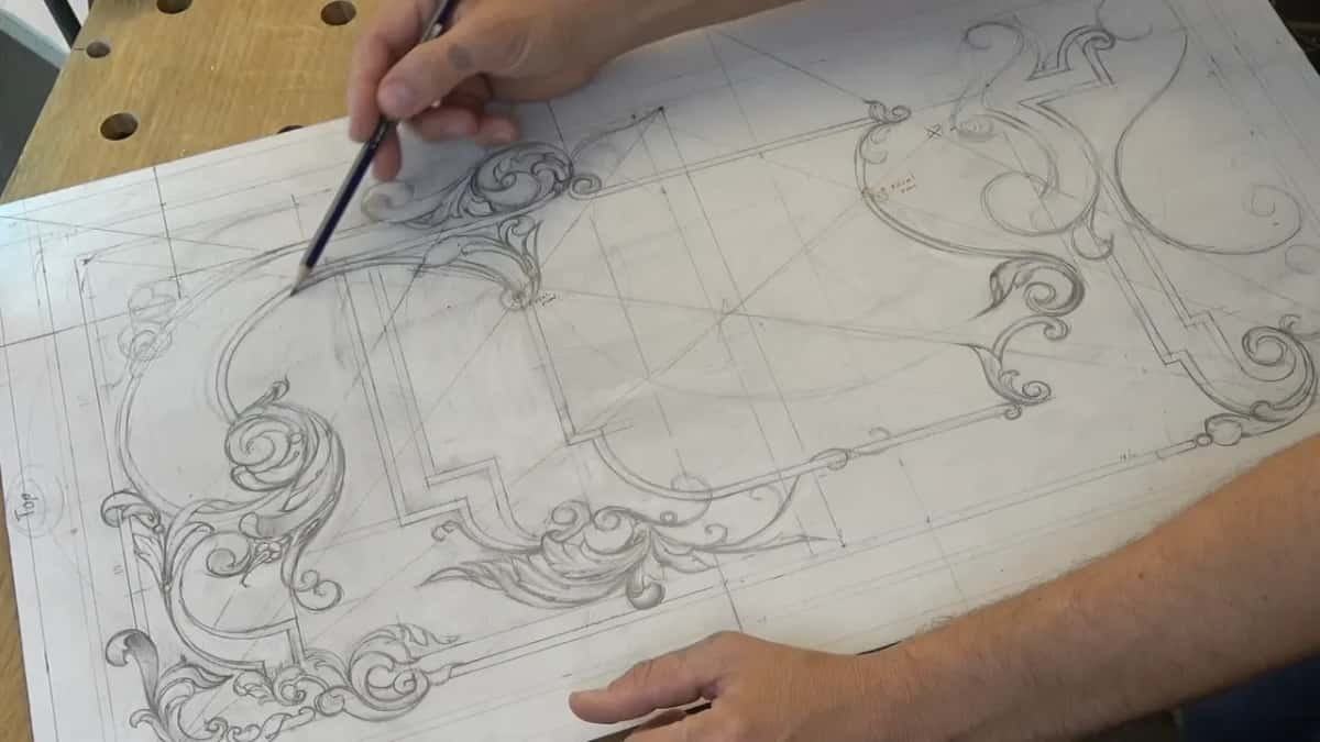 Drawing laid on a pale workbench full of dog holes, both hands at the sheet