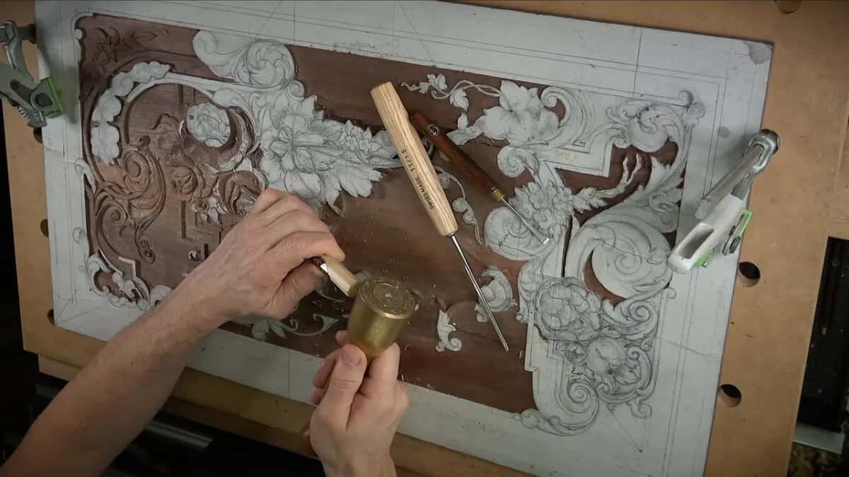 Brass mallet raised above a chisel, two Swiss Made handles lying on the panel beside them, shavings scattered