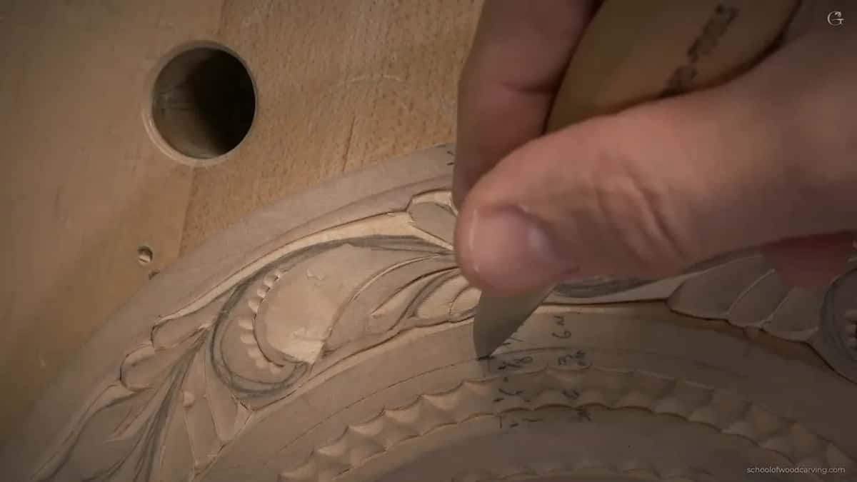 A thumb guides the blade onto the line under the leaf band, beside penciled numbers