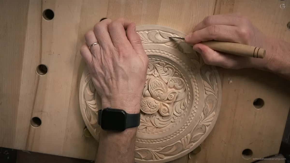 Overhead, a hand wearing a watch holds the plate while a pale-handled knife works the top of the rim