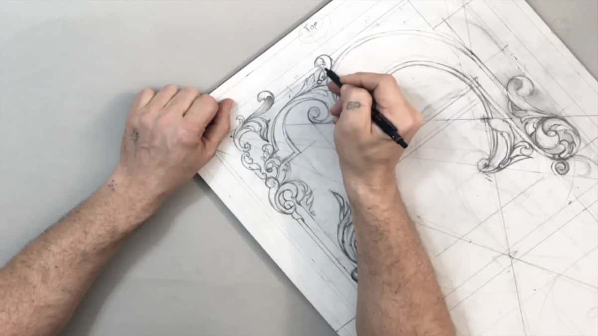 One hand pins the sheet while the other draws at the left scrolls, the word Top above them