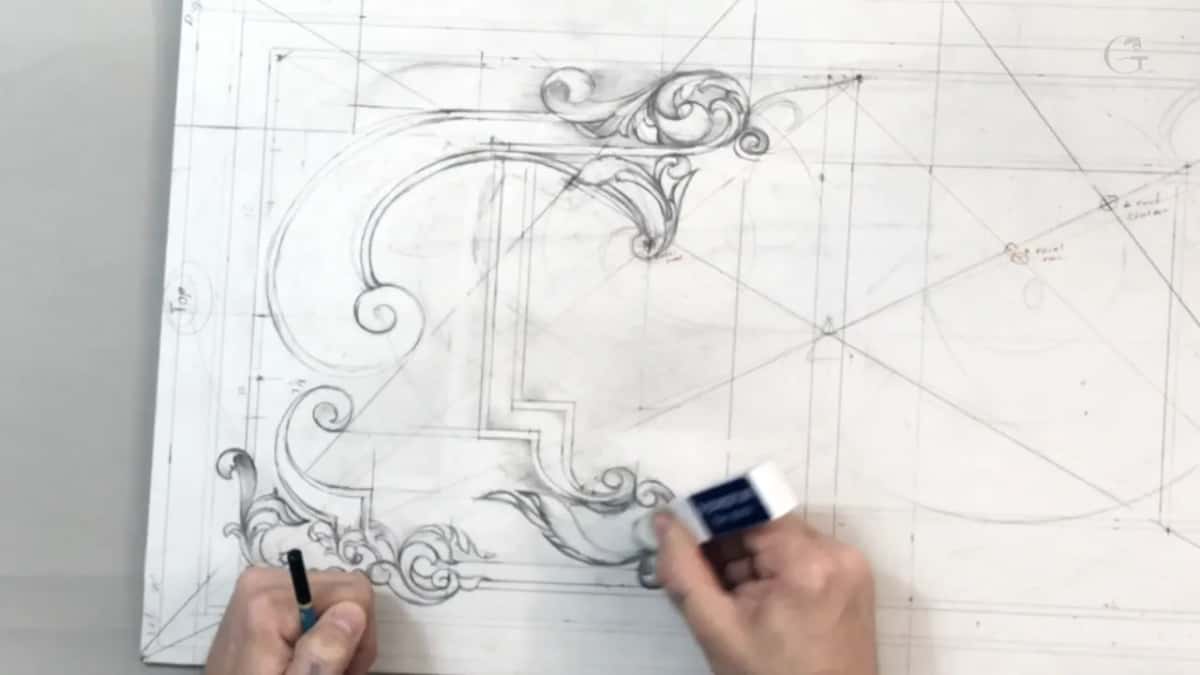 Blue eraser rubbing at the long bottom leaf while the other hand holds a pencil by the scrolls