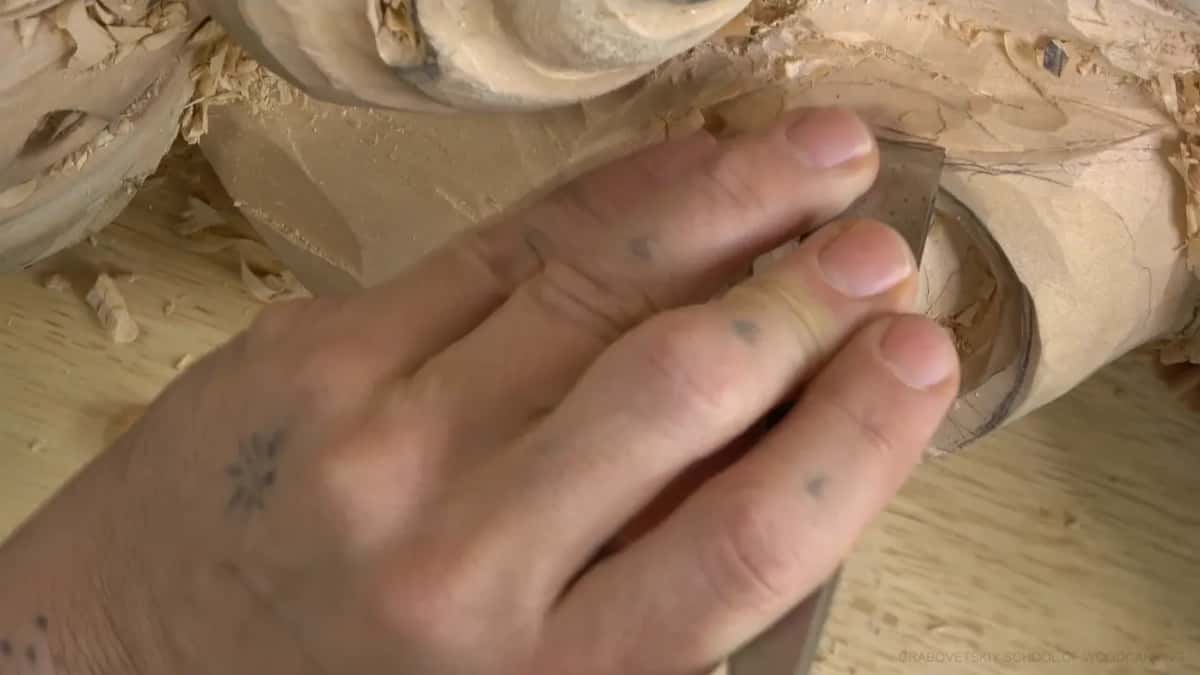 Fingers pin a flat chisel to the side of the volute.