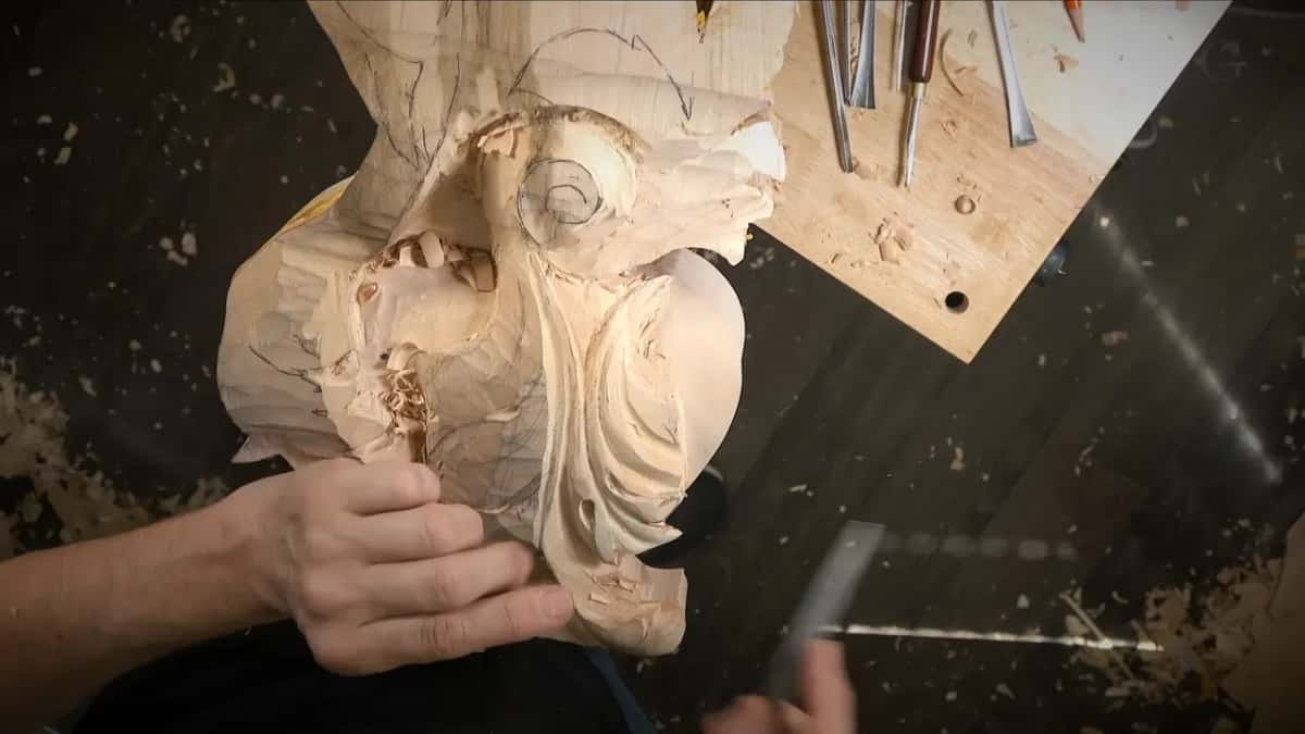 Left hand holding the big carving while a flat rasp, blurred with motion, comes in from the lower right corner