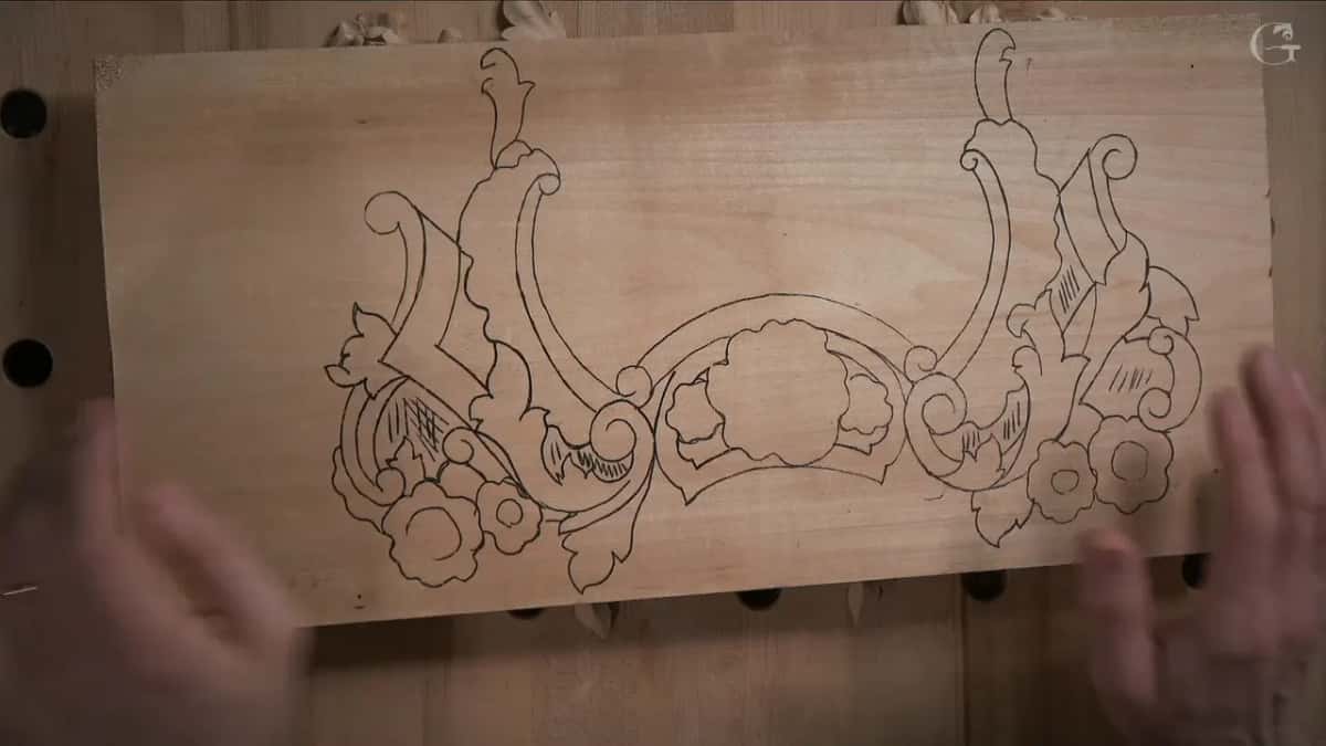 Design drawn across the basswood board, scrolls and flowers waiting to be sawn and then carved, hands holding the edges