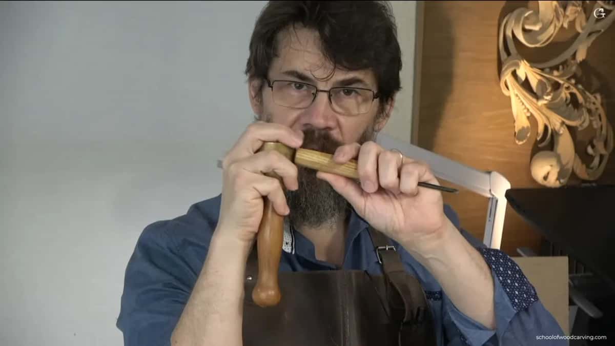 Holding a mallet in one hand and a gouge in the other, he shows how the two meet.