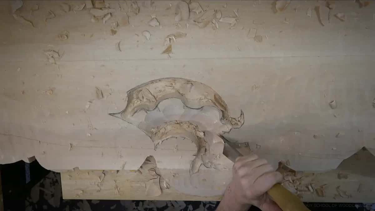 One hand drives a gouge into the lower curve of the shell, the upper part already hollowed
