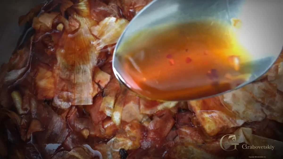 Onion husks boiling in a pan with a spoon lifting the liquid, already amber after a few minutes on the stove.