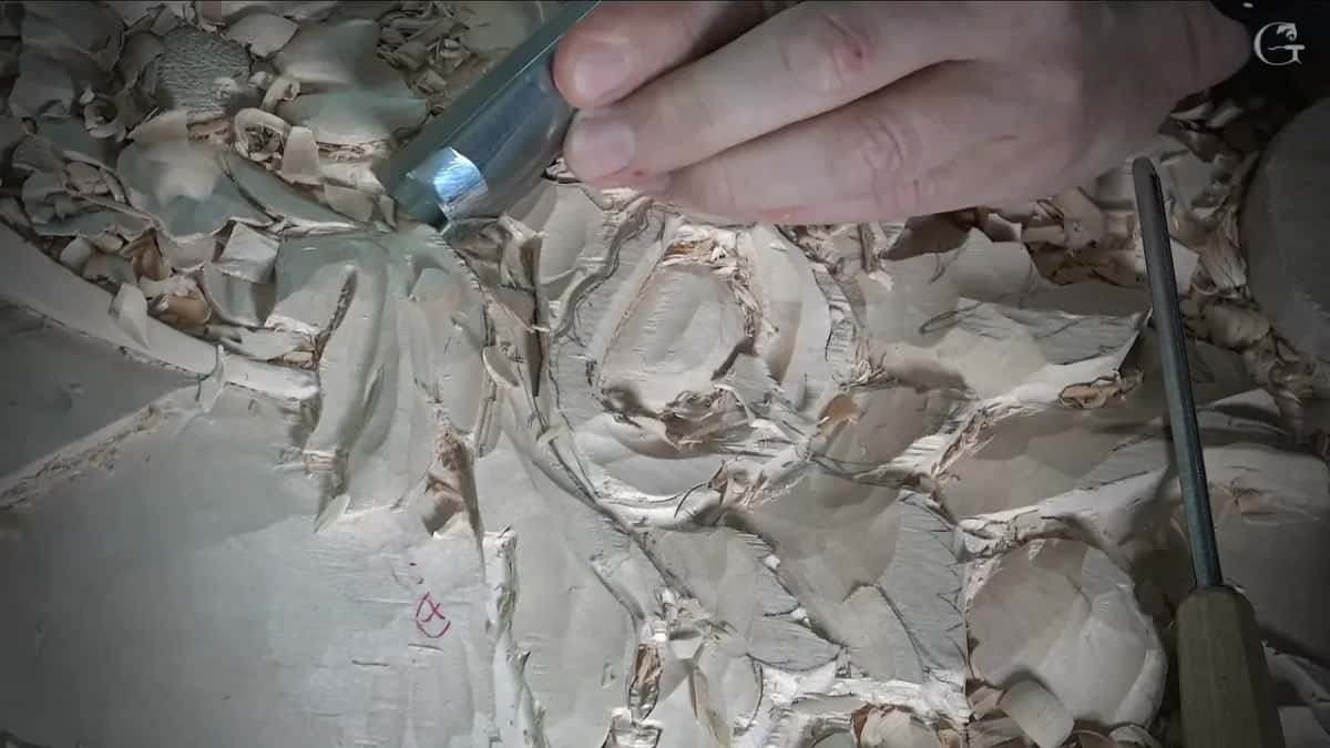 Wide gouge at work between two leaves, a second long tool lying across the right side