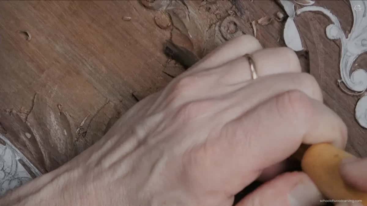 A ringed hand with a pale handled gouge rolling one lobe of the leaf under its neighbour.