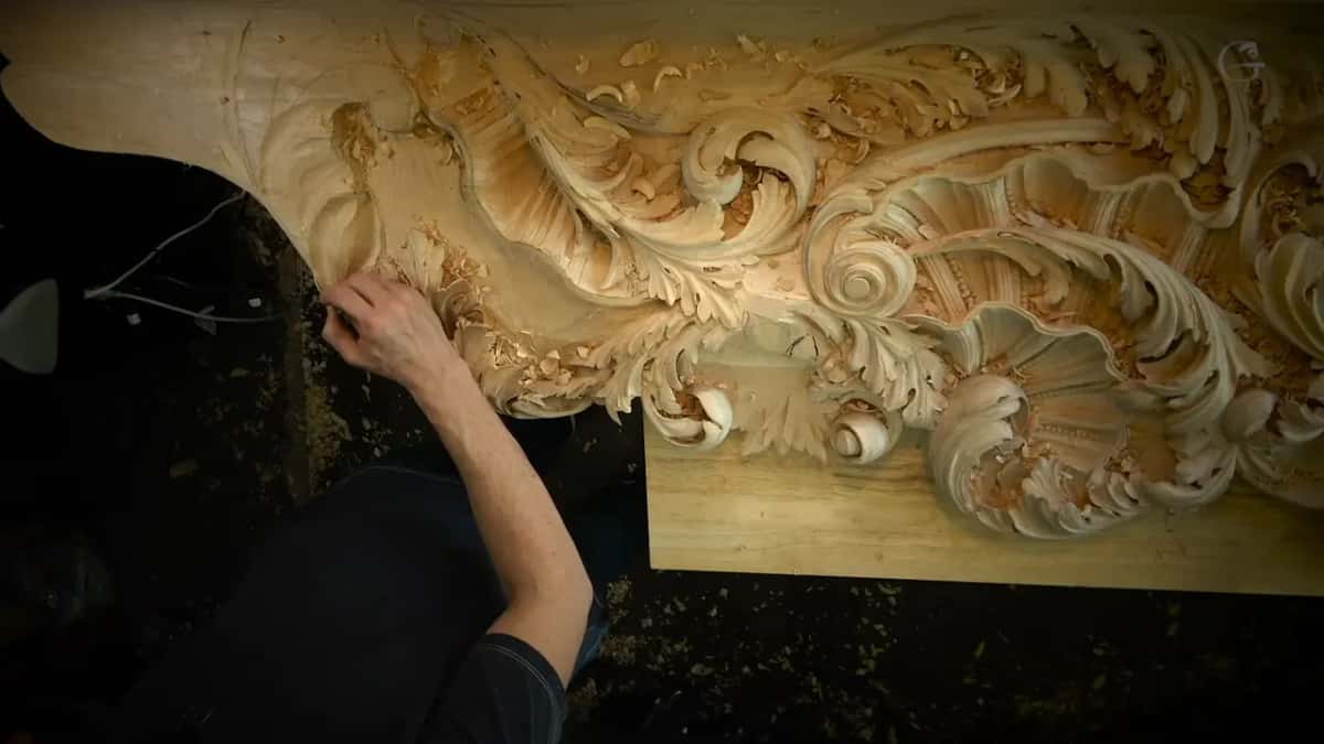 The whole board Looking down on the full board, scrolls and shell forms already carved, one arm reaching in from the left