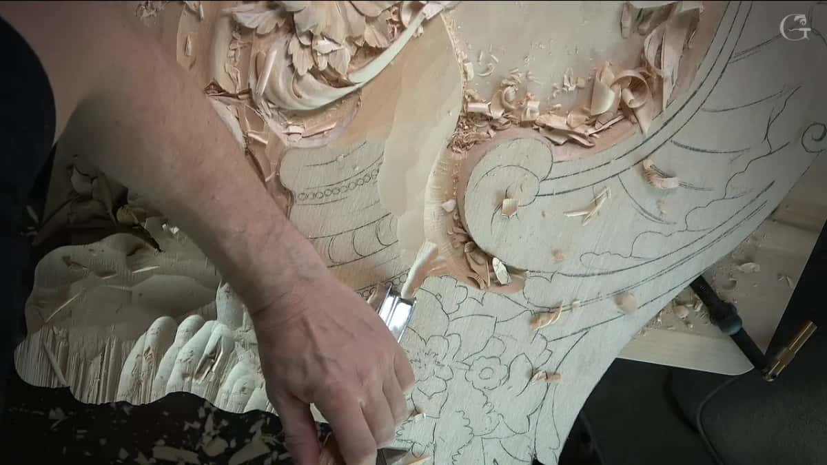 Short gouge held near the carved leaves at the lower edge of the panel