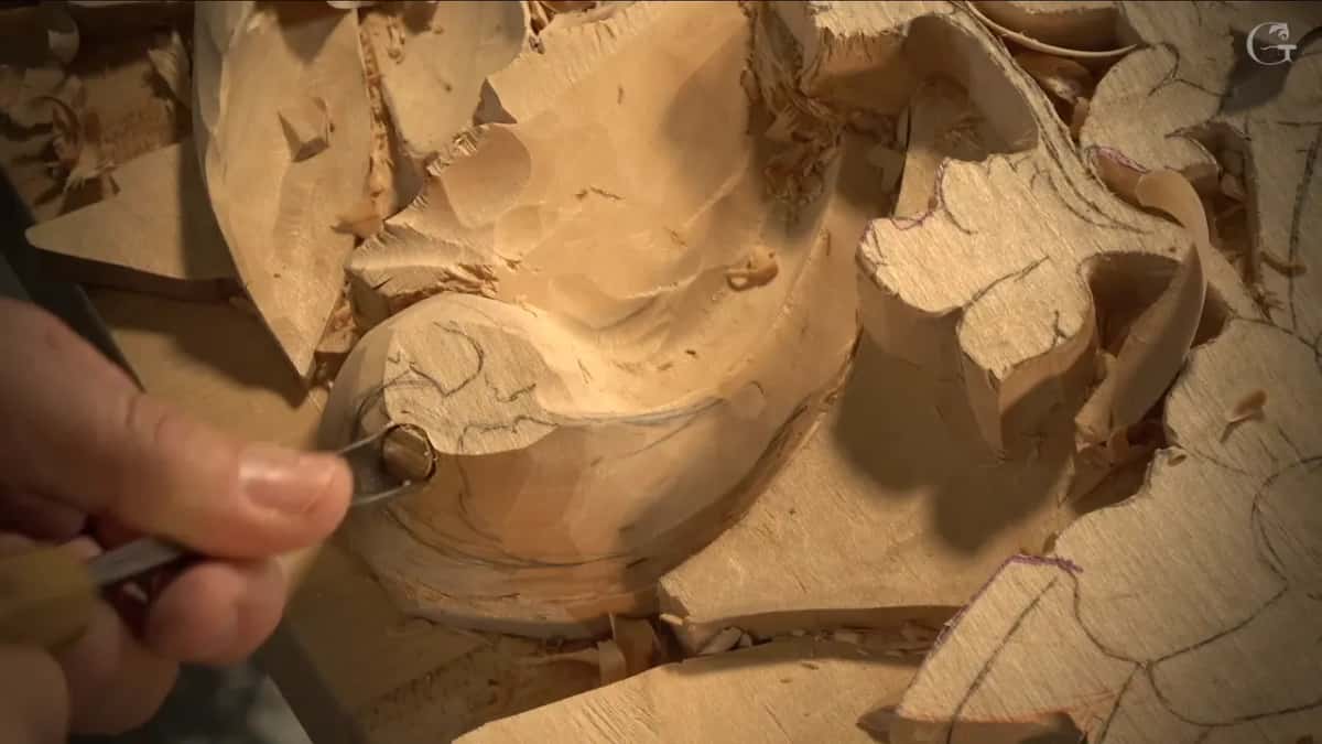 Fingertips guide a small gouge so its edge points into the curl of the scroll