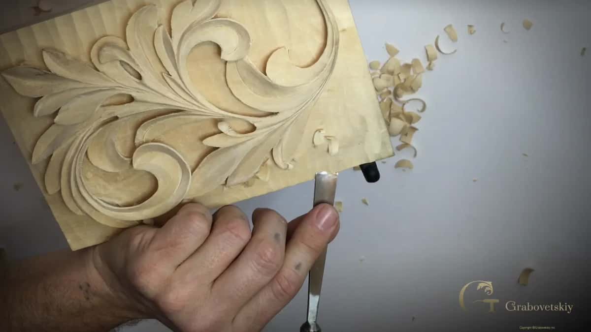 One hand holds a gouge under the bottom edge while the carved leaf fills most of the frame