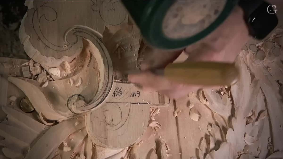 A green mallet strikes the end of a chisel held upright