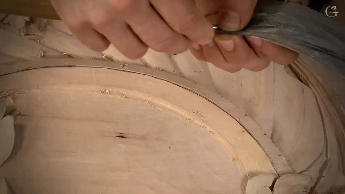Both hands steer a small veiner along the fine line of a carved arch