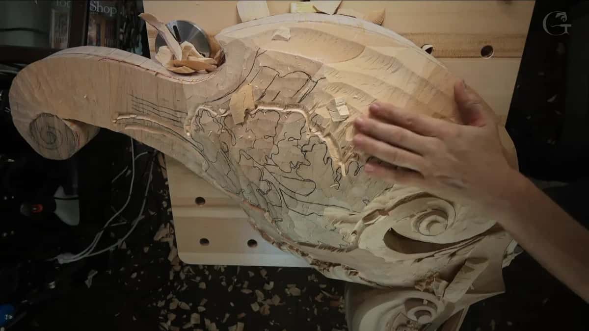 An open hand rests on the lowered wood between piles of chips, drawn lines still showing underneath