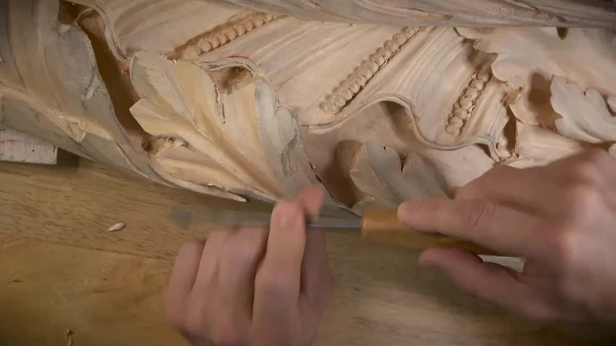 Two hands push a pale handled tool along the underside of a leaf
