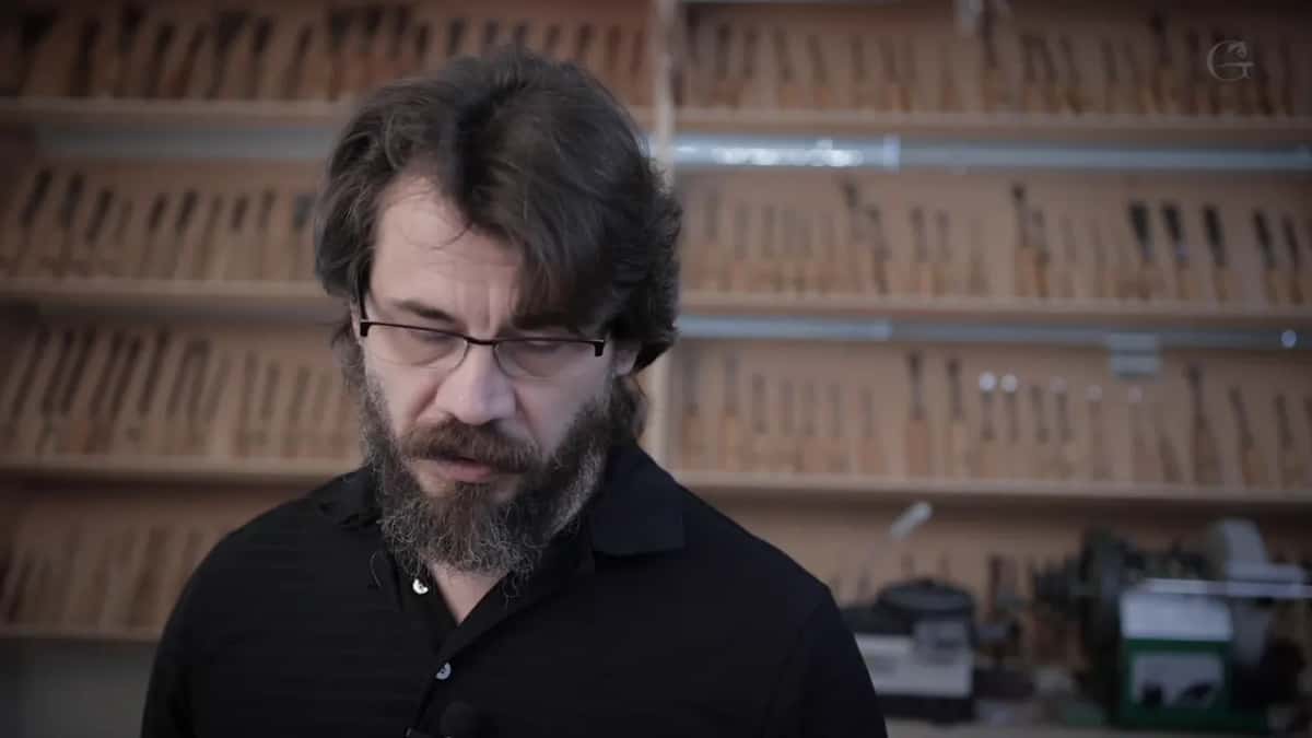 Alexander at his bench with racks of gouges filling the wall behind him, using almost none of them.