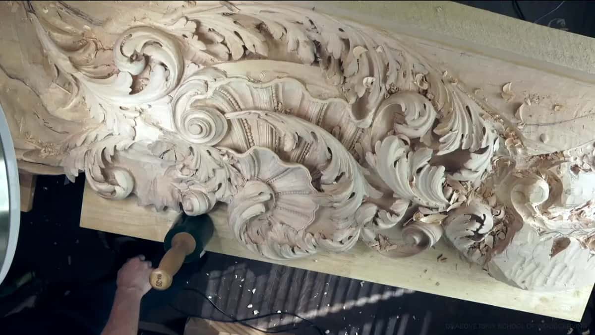 Carved ceiling board lying flat on a pale plank, with a green mallet beside it.