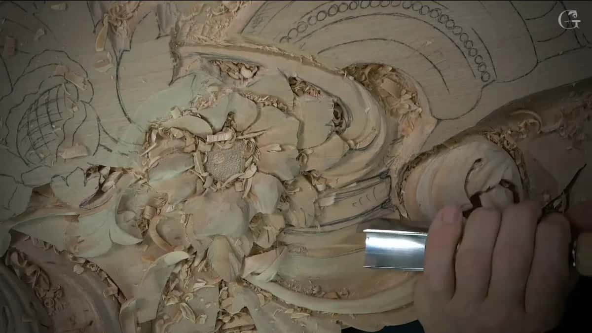 Wide silver gouge in one hand, pressed against the base of the scroll