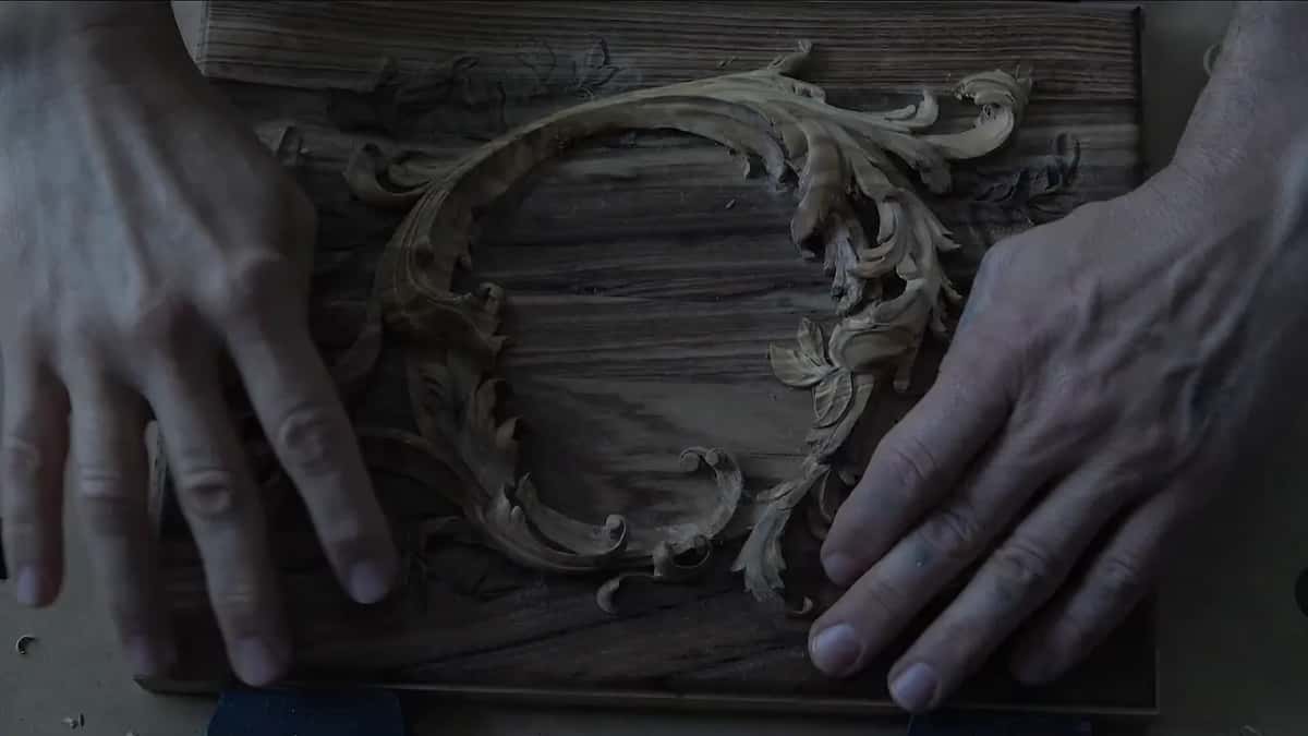 Lights off, two hands resting on the lid as the carved layer throws its shadows