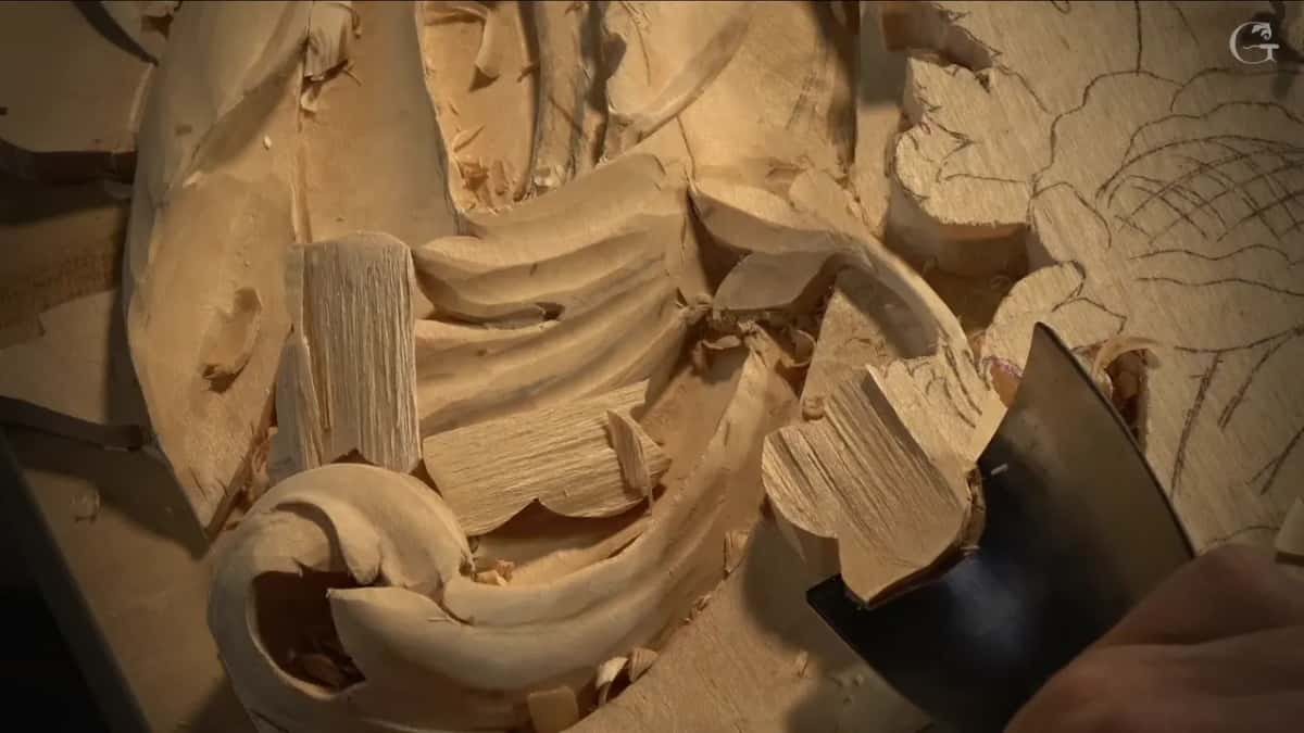 Wide flat gouge resting against the base of a leaf, square chips of wood lifted around it.